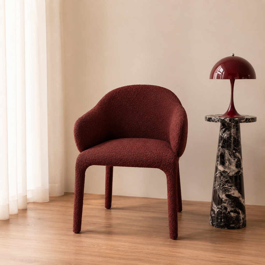 Maroon chair and black marble table against a beige wall with white curtains.
