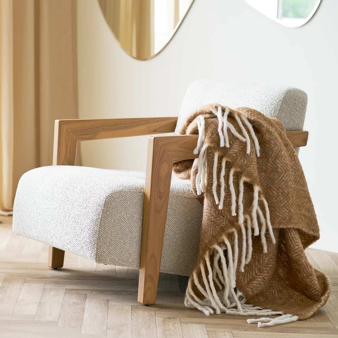 Wooden armchair with a white cushion and a brown blanket draped over it in a room setting.