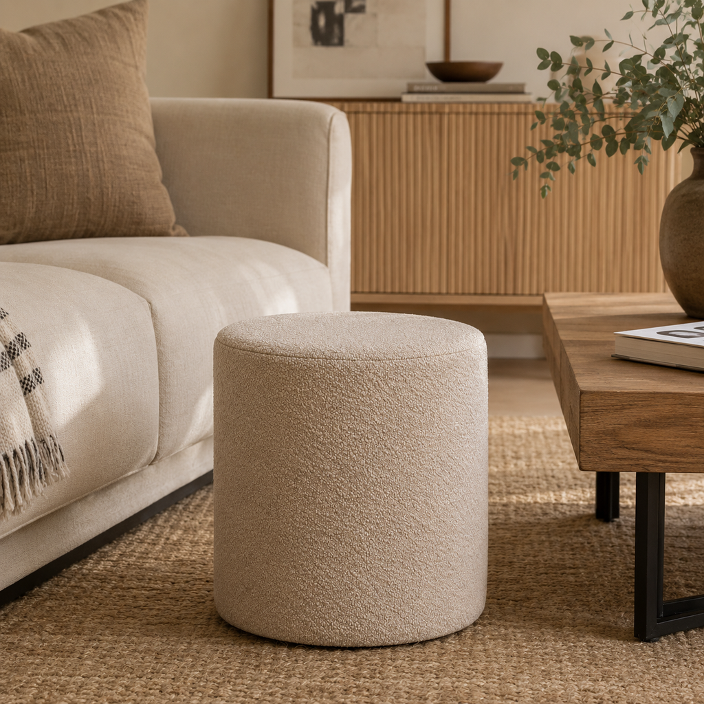 Beige ottoman in a living room setting with a sofa, coffee table, and decorative items.