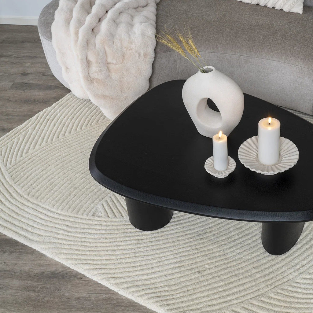 Black triangular coffee table with decorative items on a living room rug.