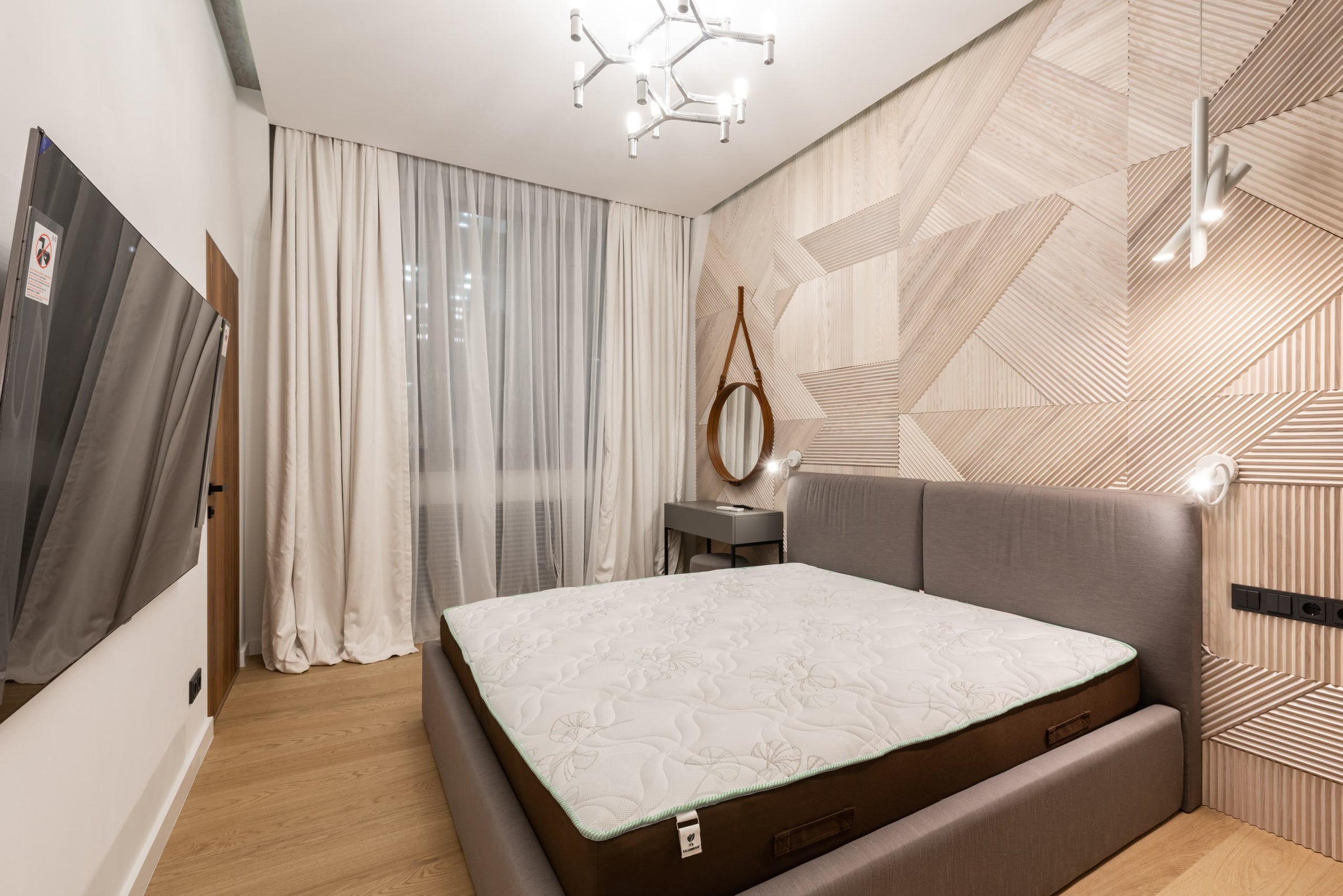A bedroom with a low upholstered bed against a geometric timber wall