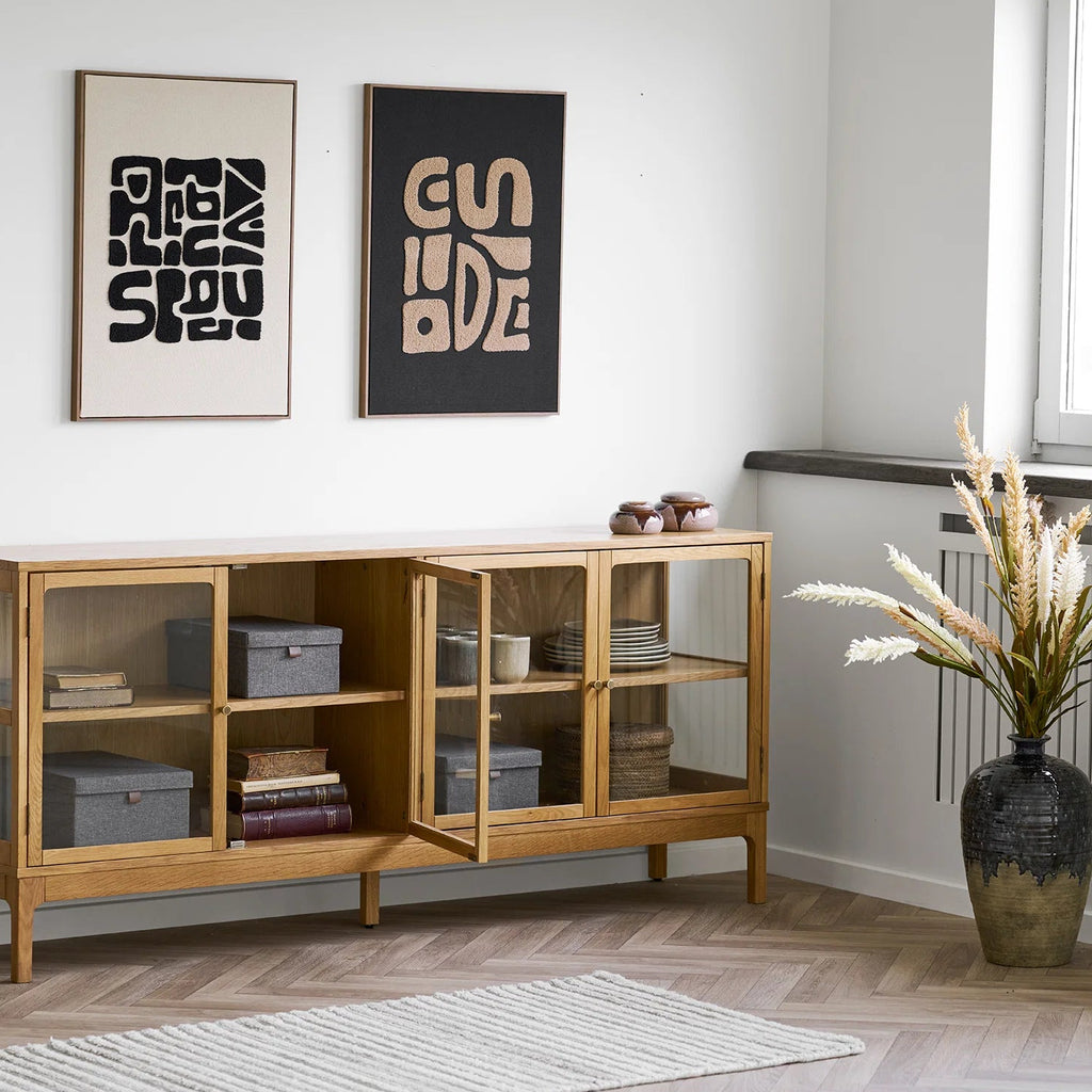 Wooden cabinet with glass doors in a room with two framed artworks on the wall.
