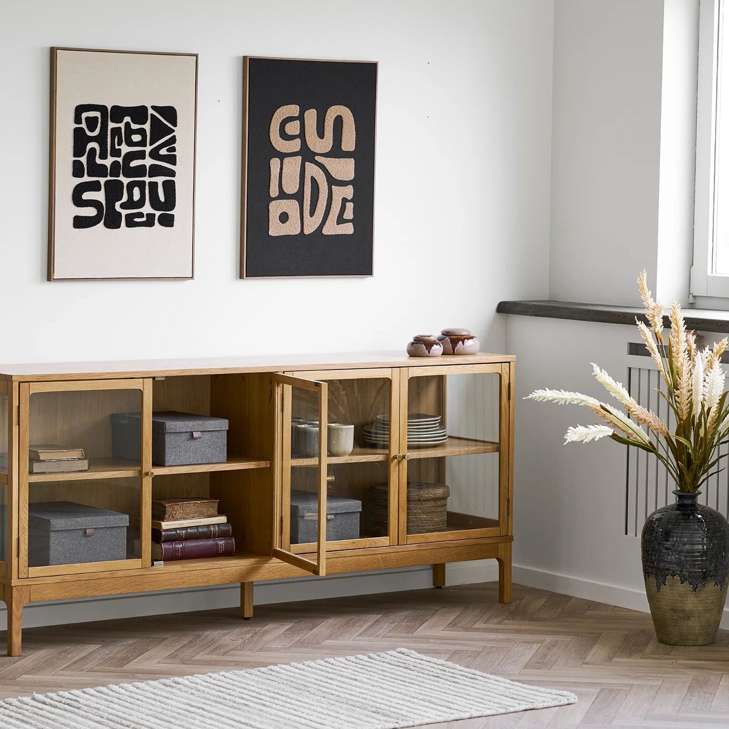 Wooden cabinet with glass doors in a room with two framed artworks on the wall.